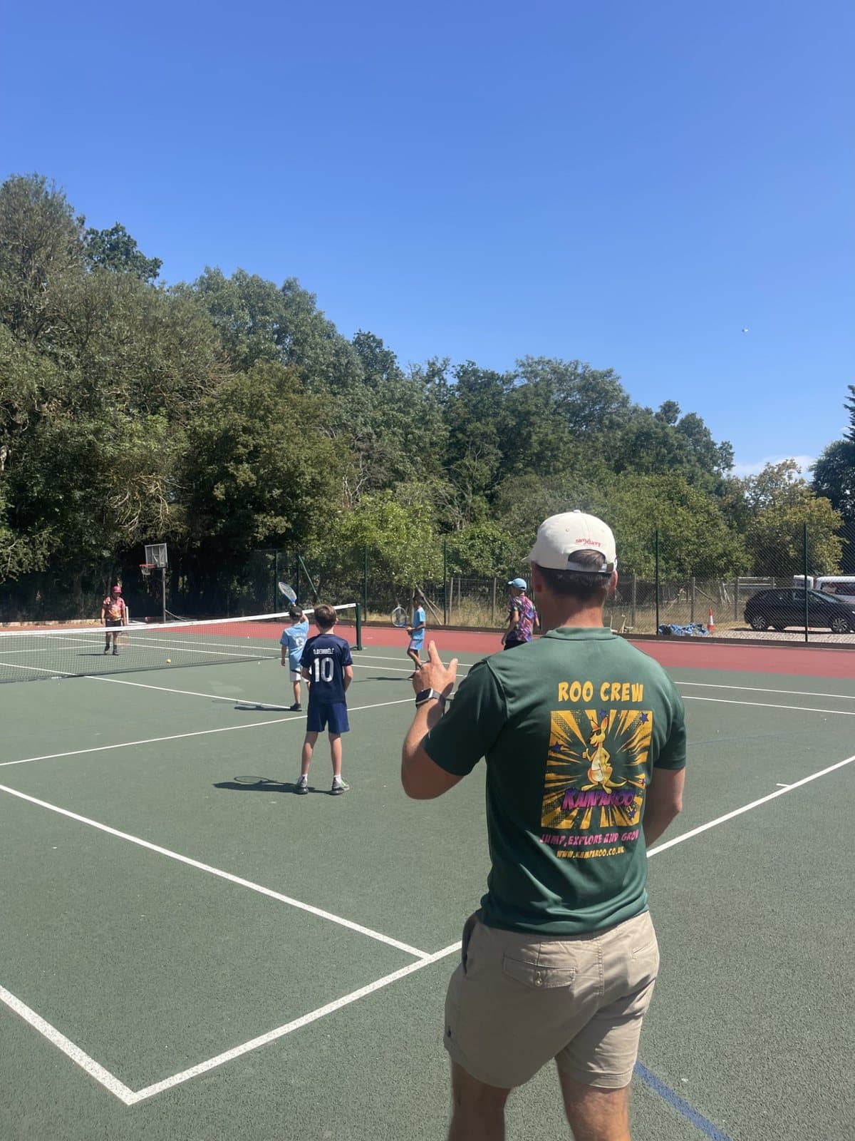 A Roo Crew coach giving a thumbs up while coaching tennis to a group of campers
