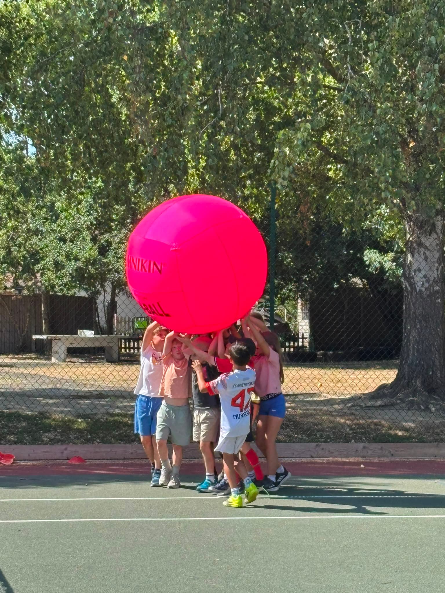 A group of campers working together to hold up a giant pink ball